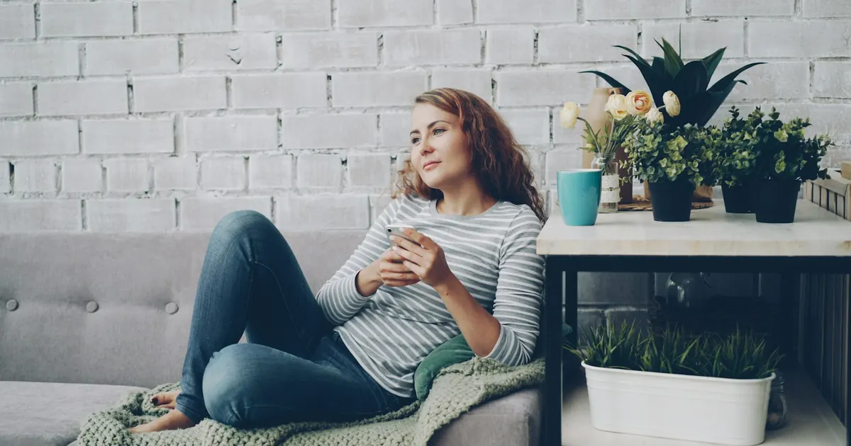 Mujer descansando en el sillón mientras revisa su celular