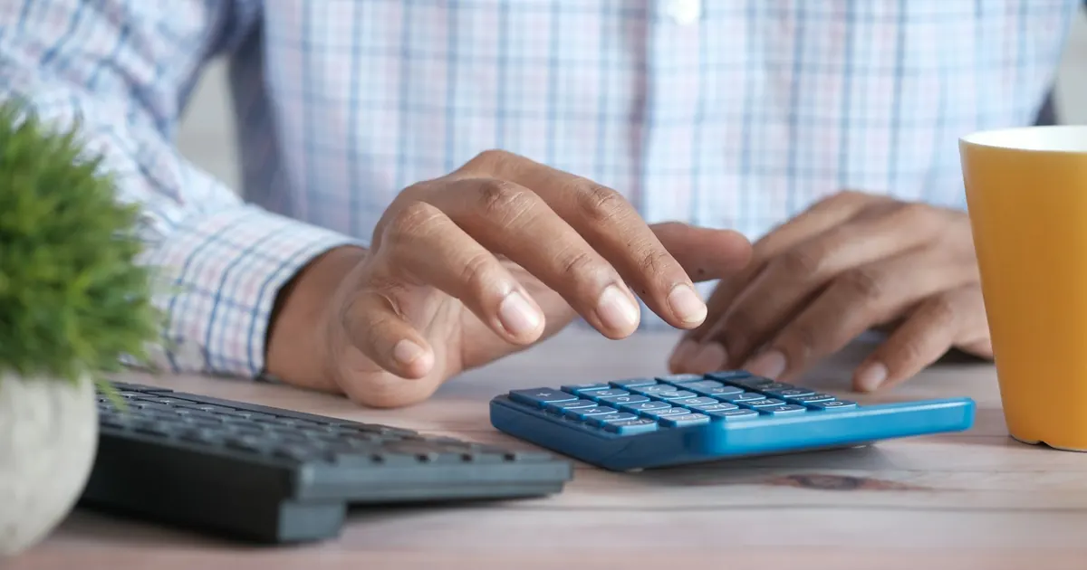 Persona usando una calculadora en un escritorio con una taza de café