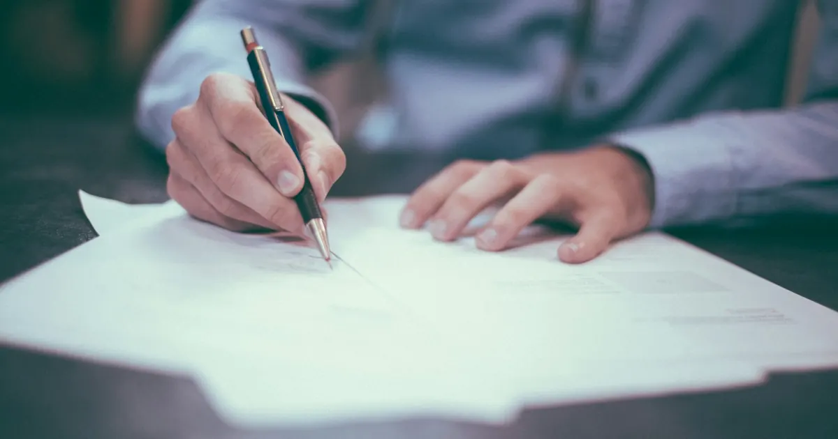 Persona firmando documentos sobre un escritorio